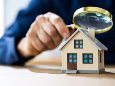 Person inspecting small model house with magnifying glass