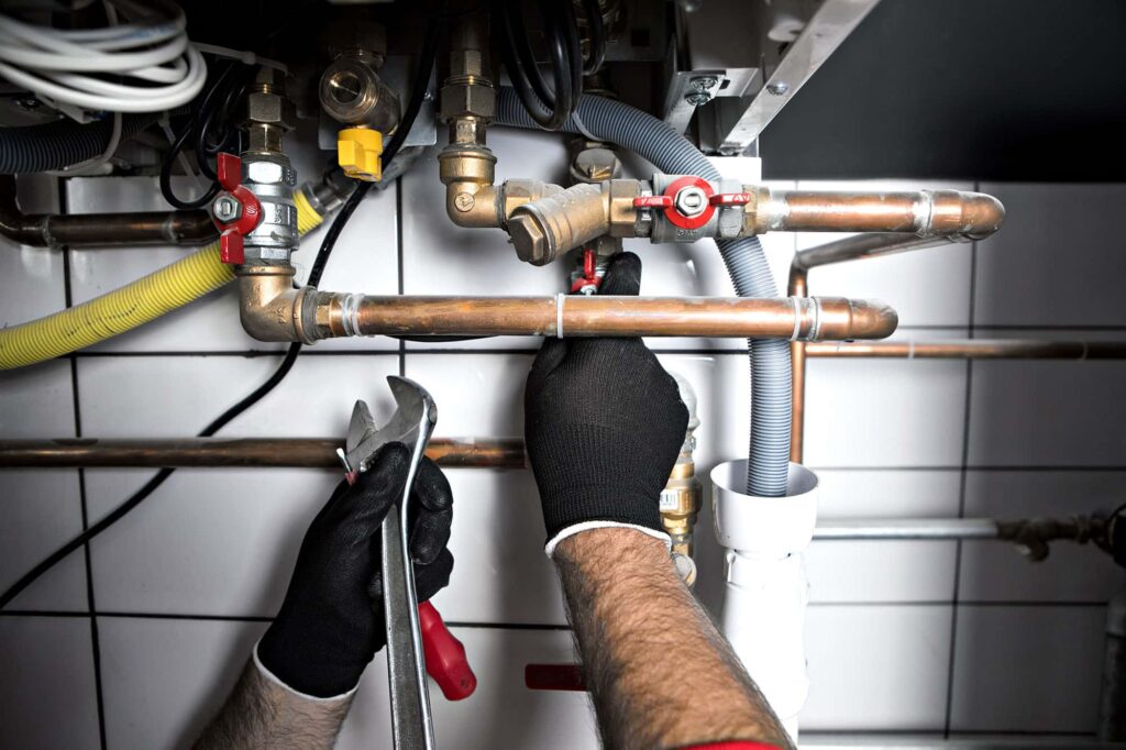 Plumber fixing pipes under sink with tools