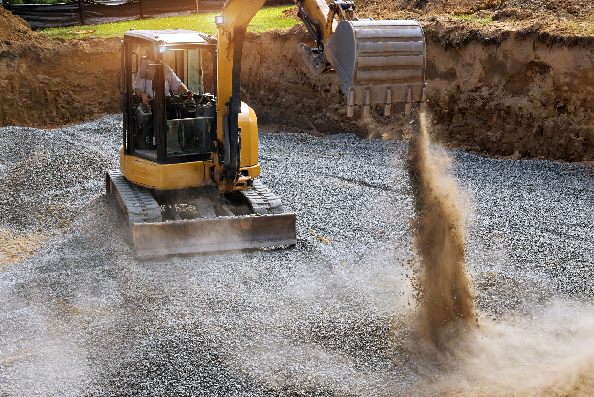 Excavator spreading gravel in construction site foundation pit