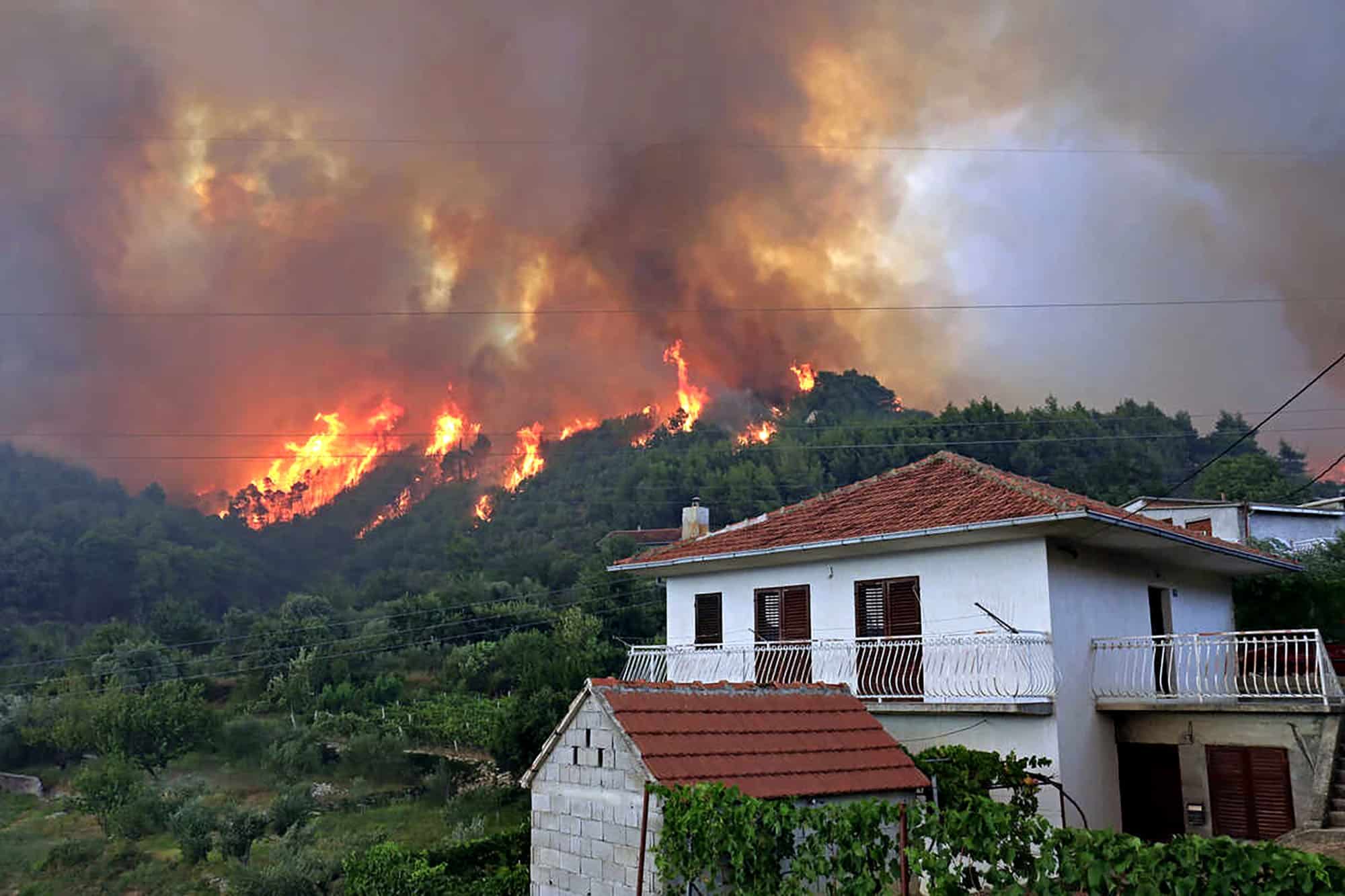 Wildfire advancing towards a residential area with houses and dense smoke