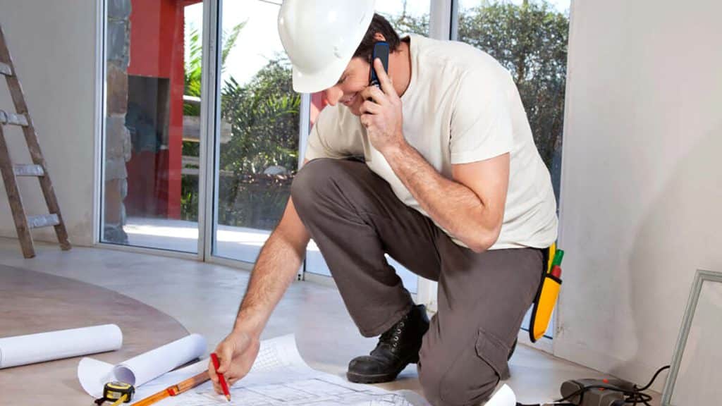 Construction worker reviewing blueprints and talking on phone indoors