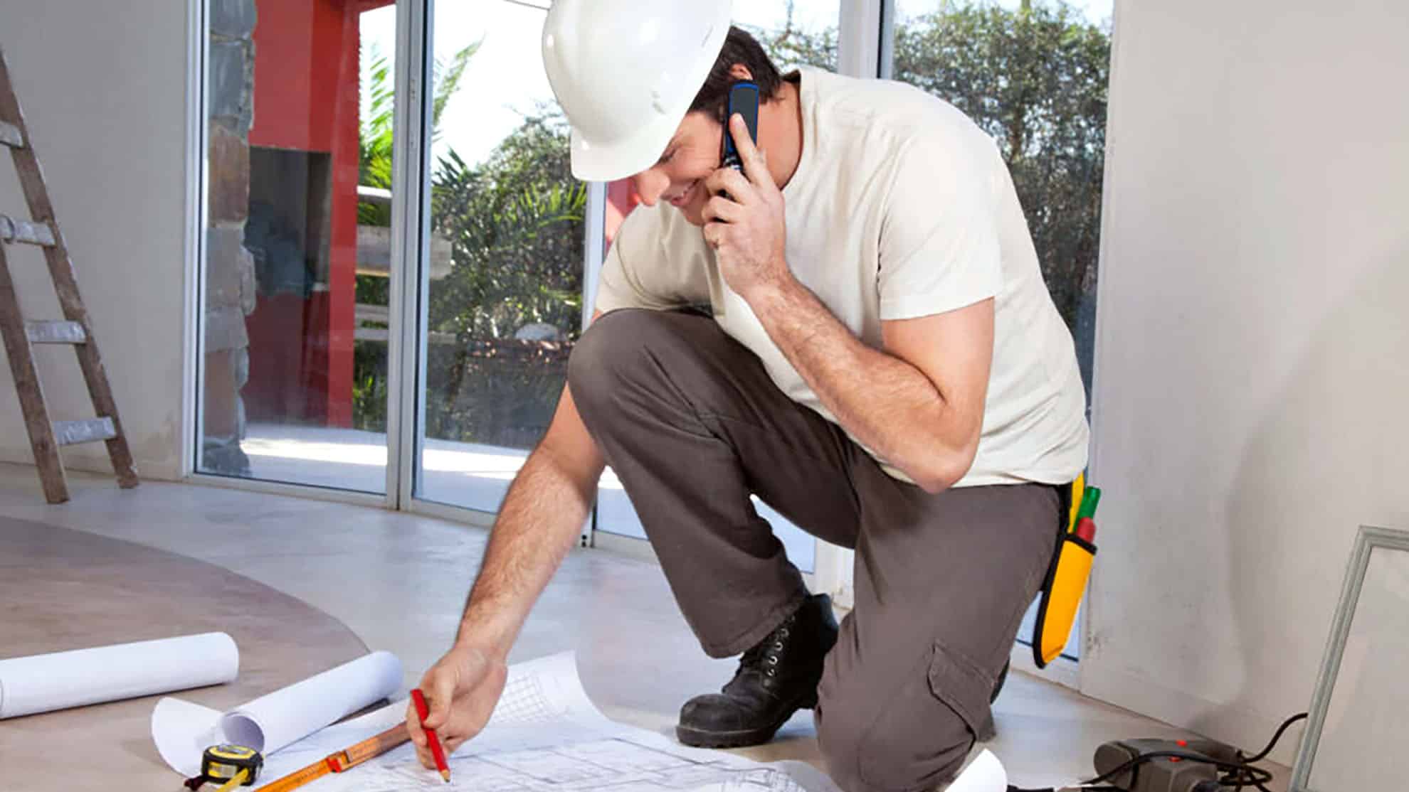 Construction worker reviewing blueprints and talking on phone indoors