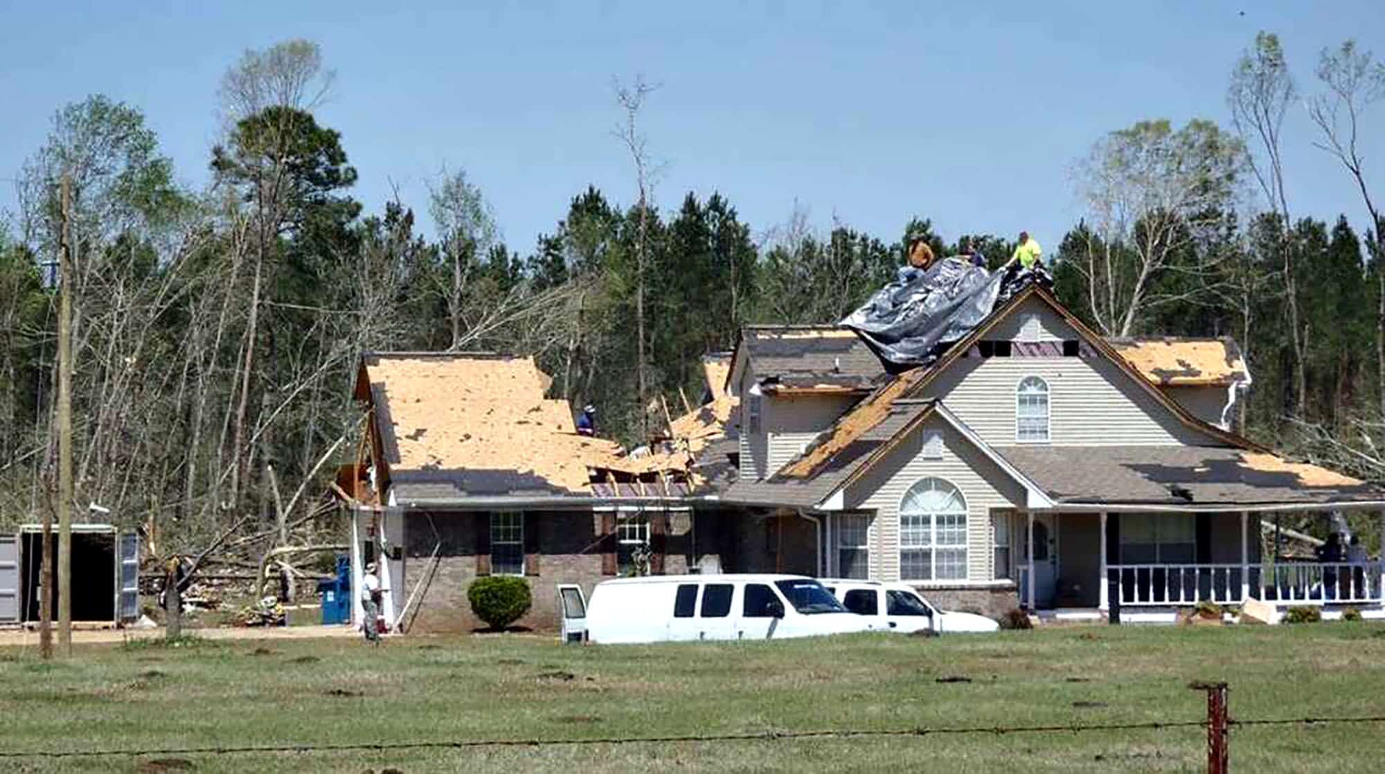 House with roof damage partially covered by tarp after storm
