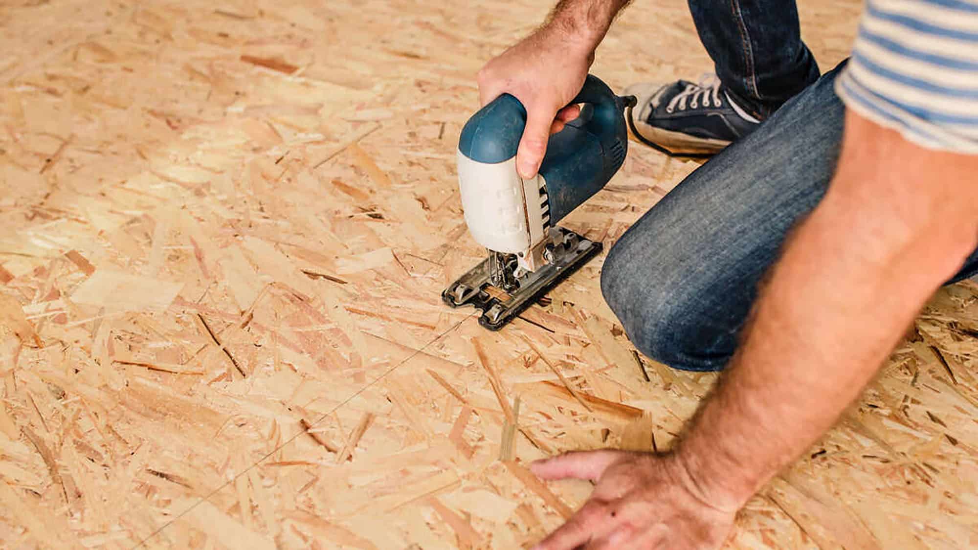 Man using a jigsaw to cut plywood flooring in renovation project