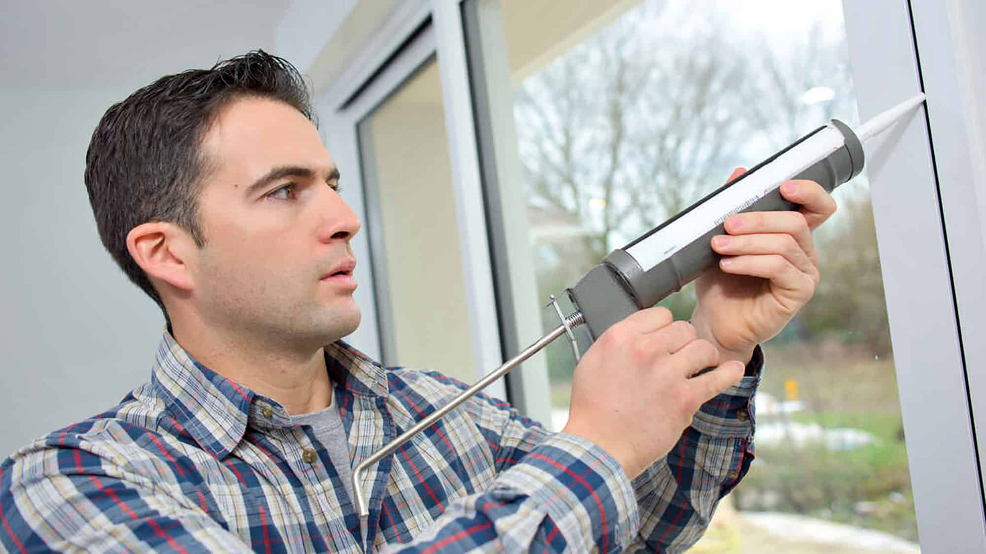 Man applying sealant to window frame using a caulking gun