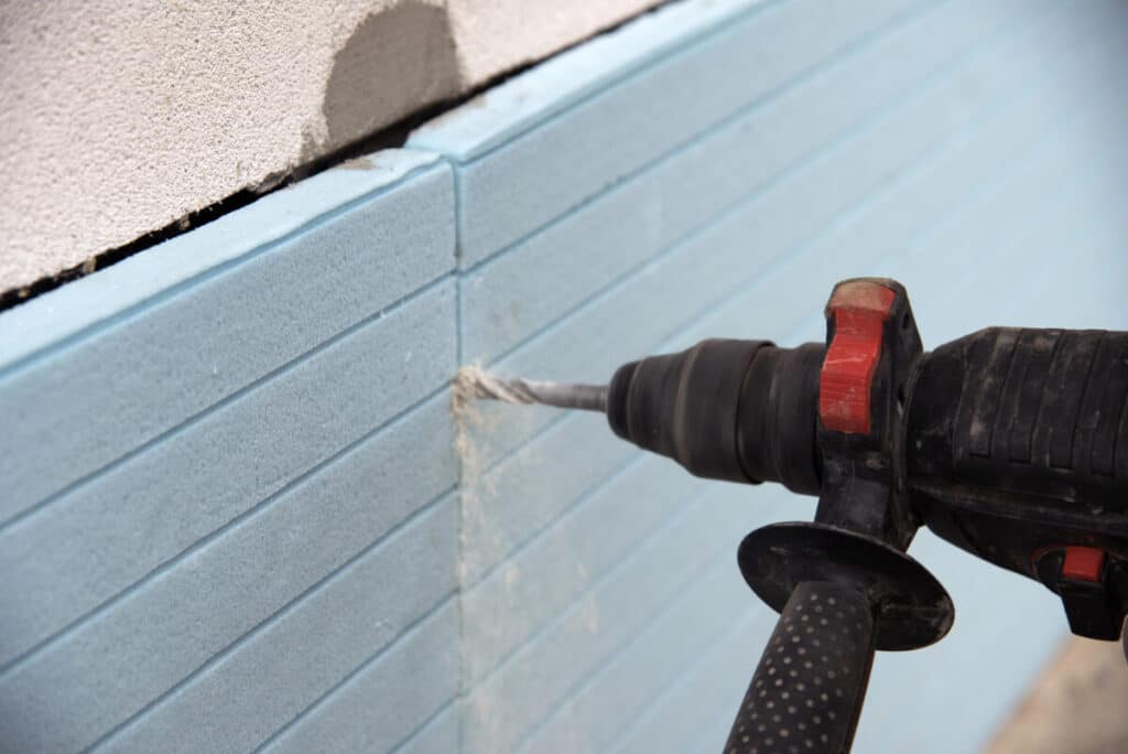 Power drill drilling into blue insulated wall panel