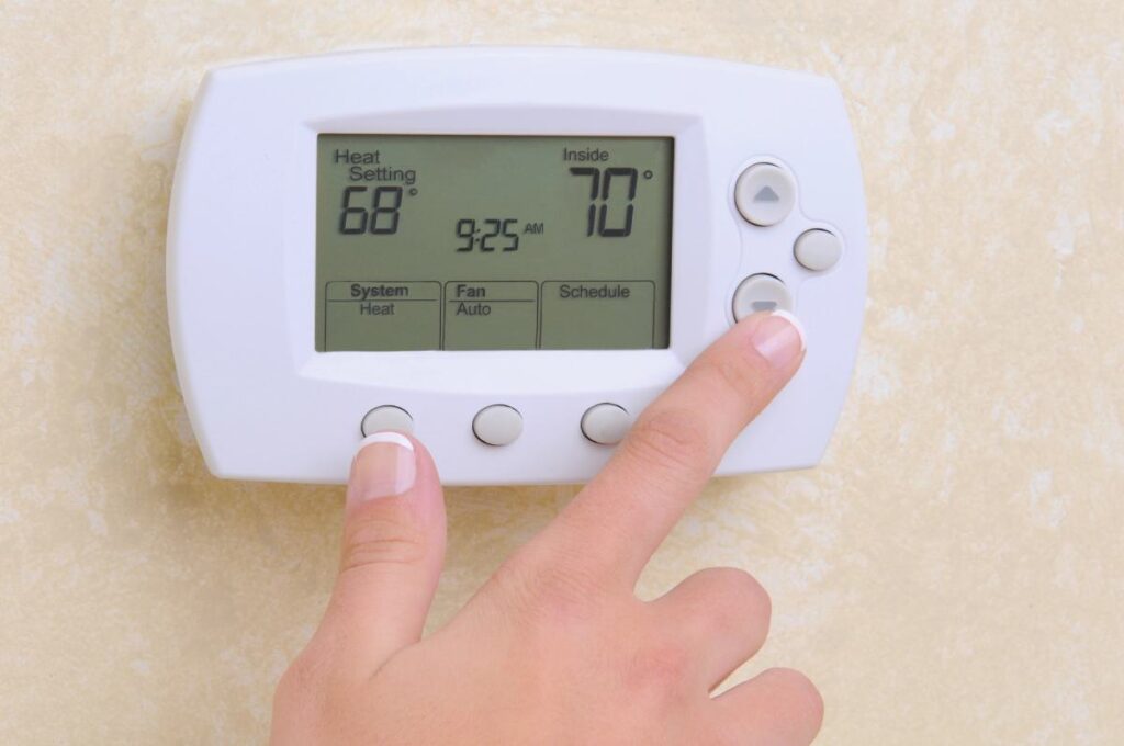 Hand adjusting home thermostat displaying 68 degrees setting