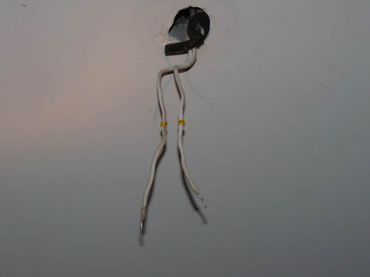 Exposed electrical wires protruding from a ceiling hole for repair