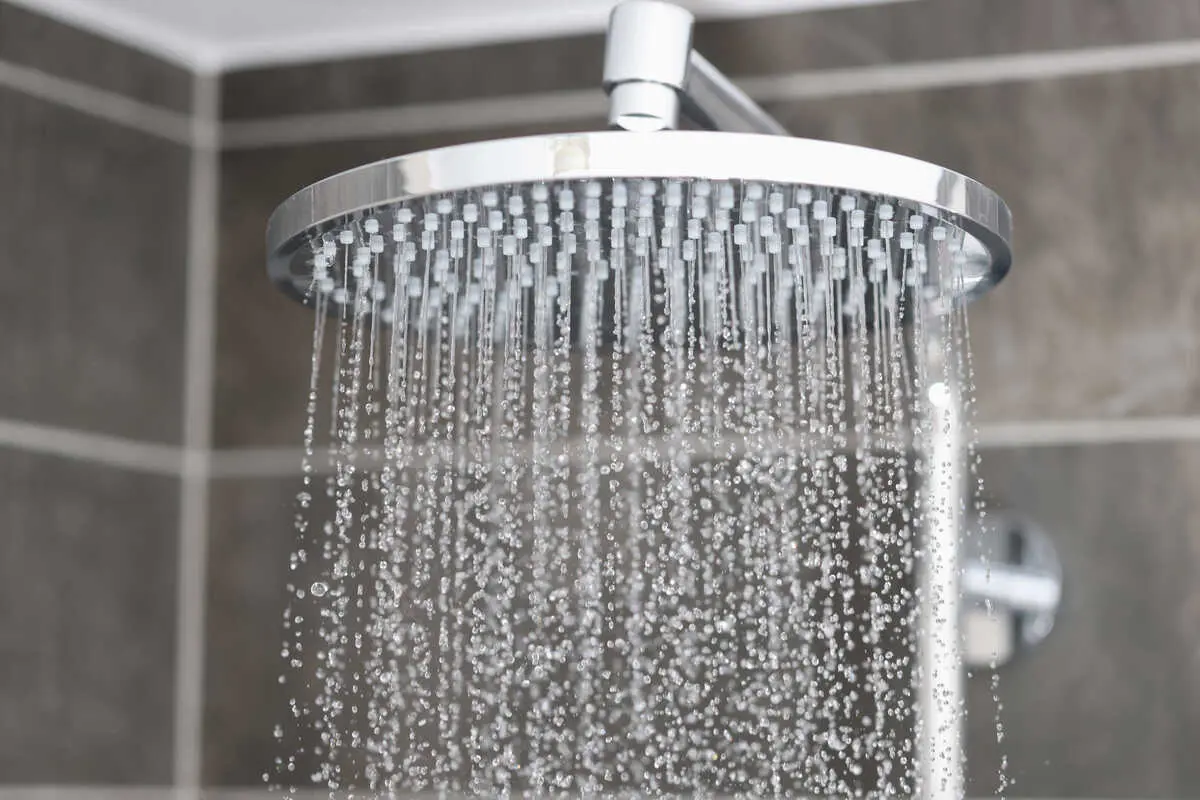 Modern chrome showerhead with water spraying in a tiled bathroom