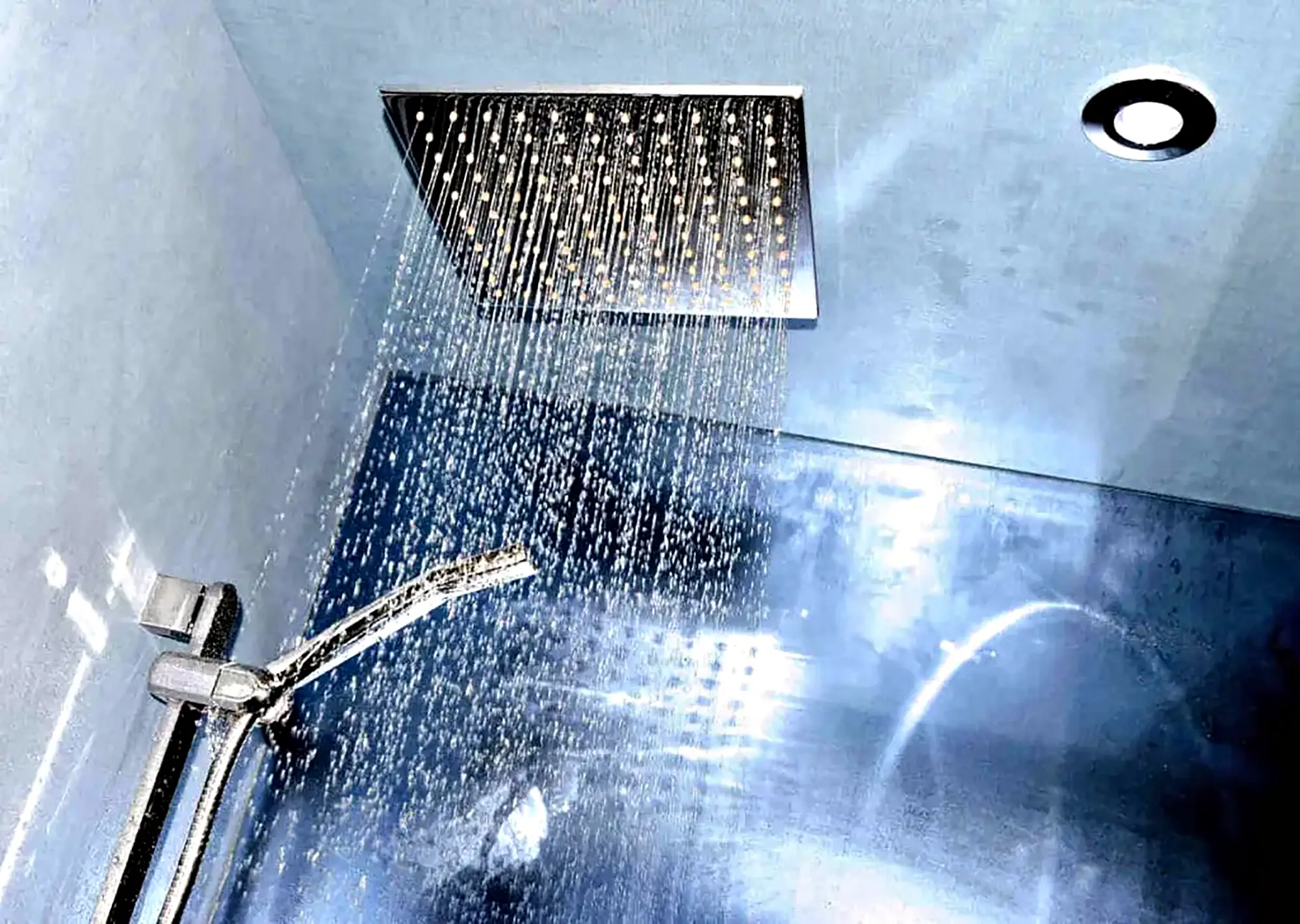 Modern square rain showerhead with flowing water in a blue-tiled bathroom