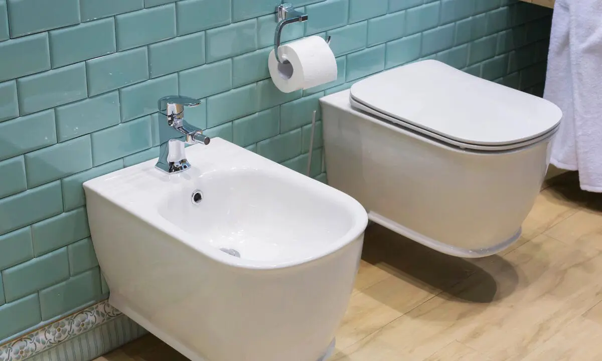 Modern bidet and toilet with teal subway tiles in bathroom