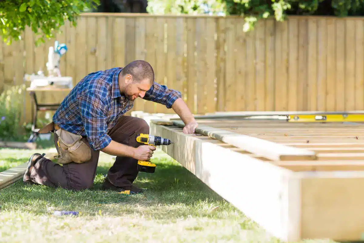Carpenter drilling wooden deck frame in backyard construction project