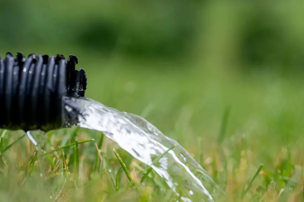 Water flowing from a black hose onto grass, illustrating drainage