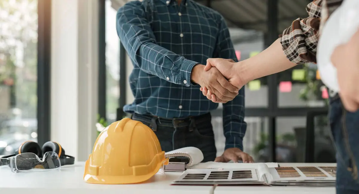 Construction professionals shaking hands over a work desk with safety gear