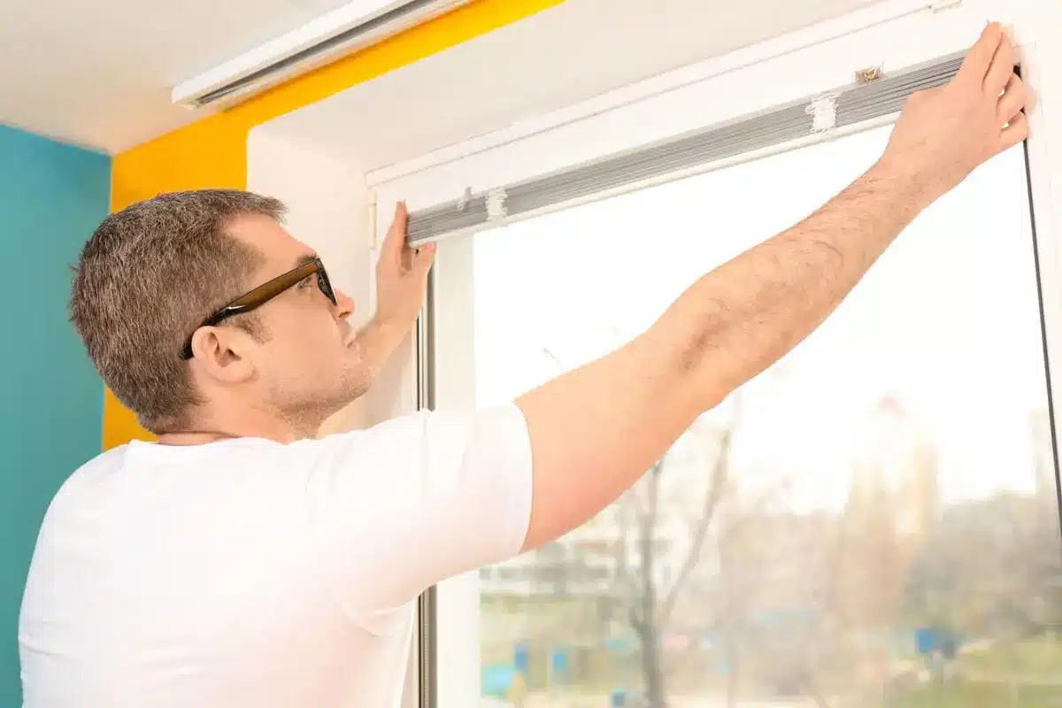 Man installing window blinds on sunny day in modern home