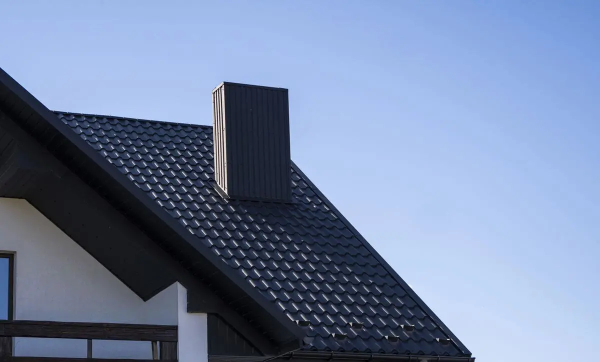 Modern house with grey metal roof and chimney under clear blue sky
