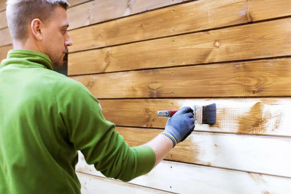 Man painting wooden fence with white paint outdoors