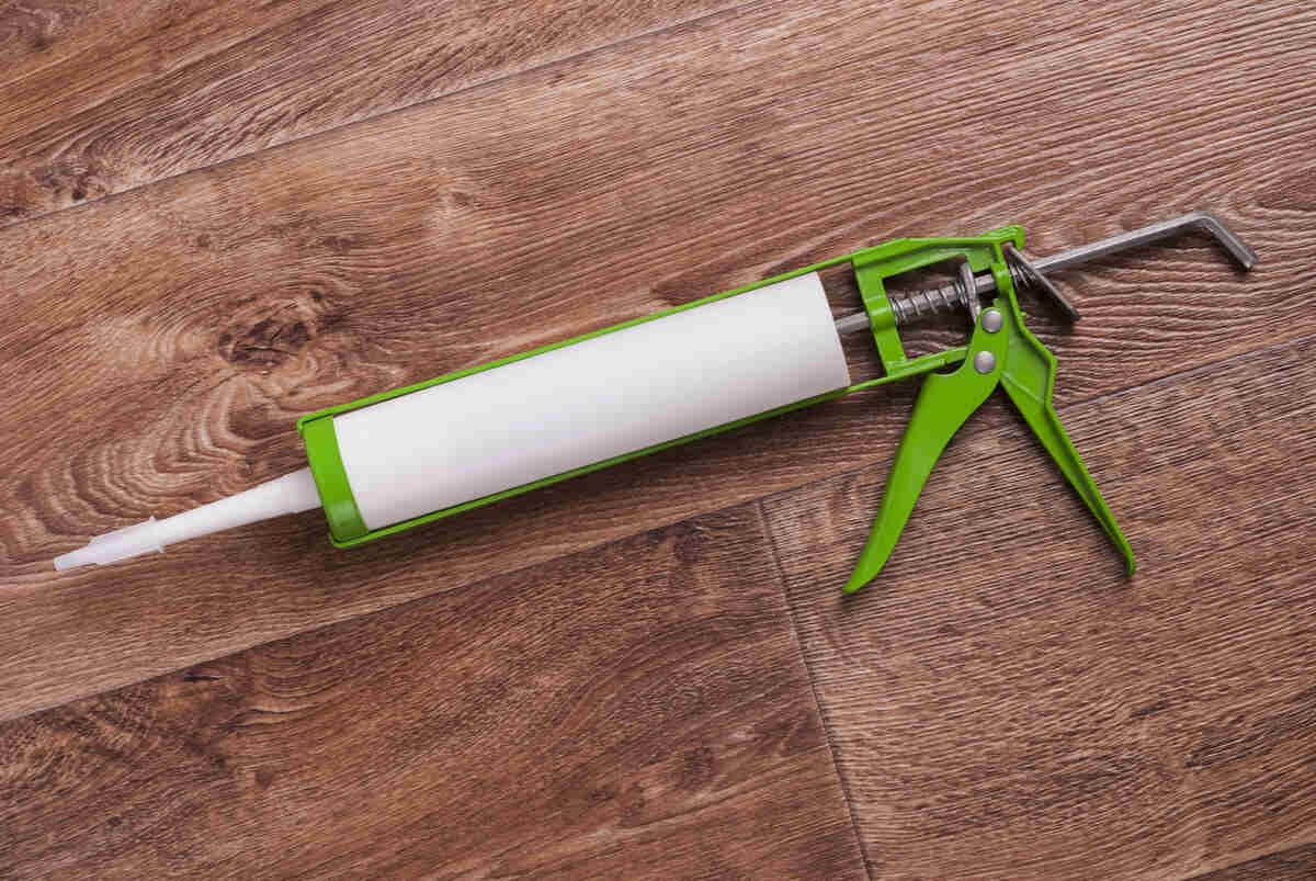 Green caulking gun on wooden floor surface