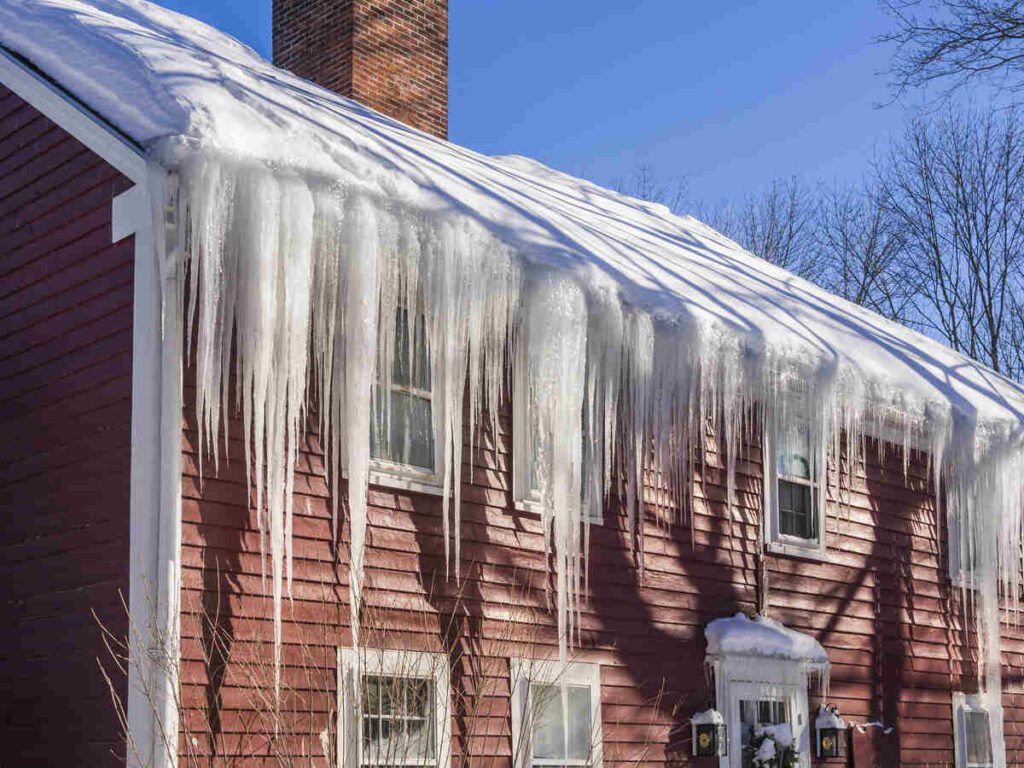 Historic red house with large icicles on the roof in winter sunlight