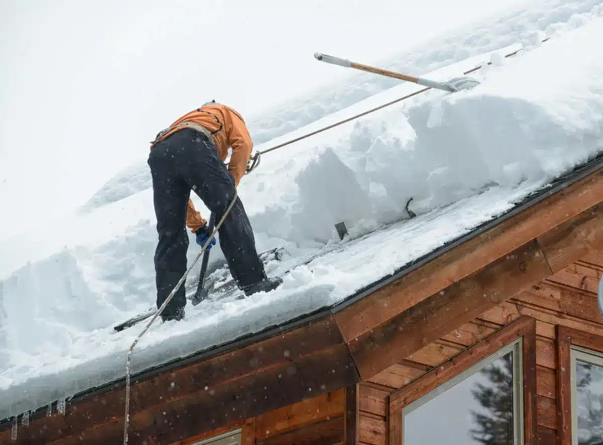 Worker removing snow from a sloping roof on a wooden house