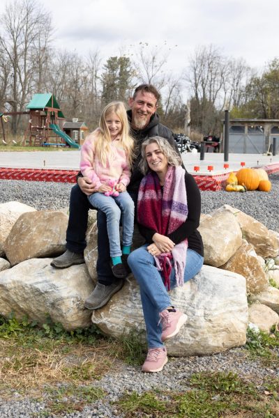 Family sitting on rocks at a playground with pumpkins and trees